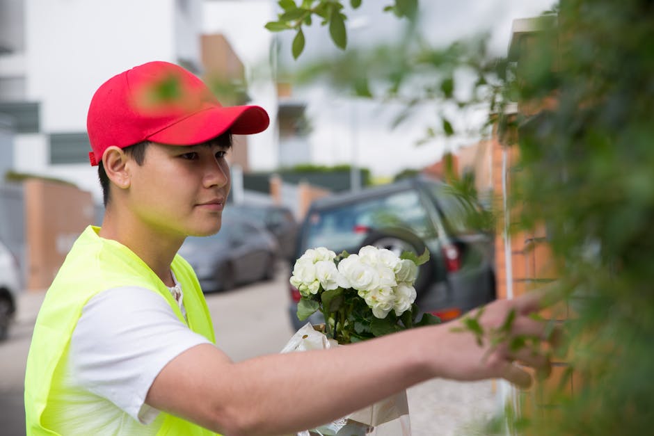 A young male flower delivery courier wearing a red cap and fluorescent yellow vest is seen outdoors, holding a bouquet of fresh white hydrangeas wrapped in white paper. He is placing the bouquet again